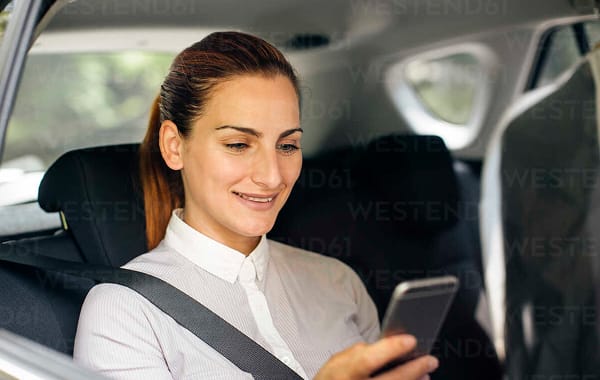 Vrouw op de achterbank van een auto kijkt op haar smartphone.