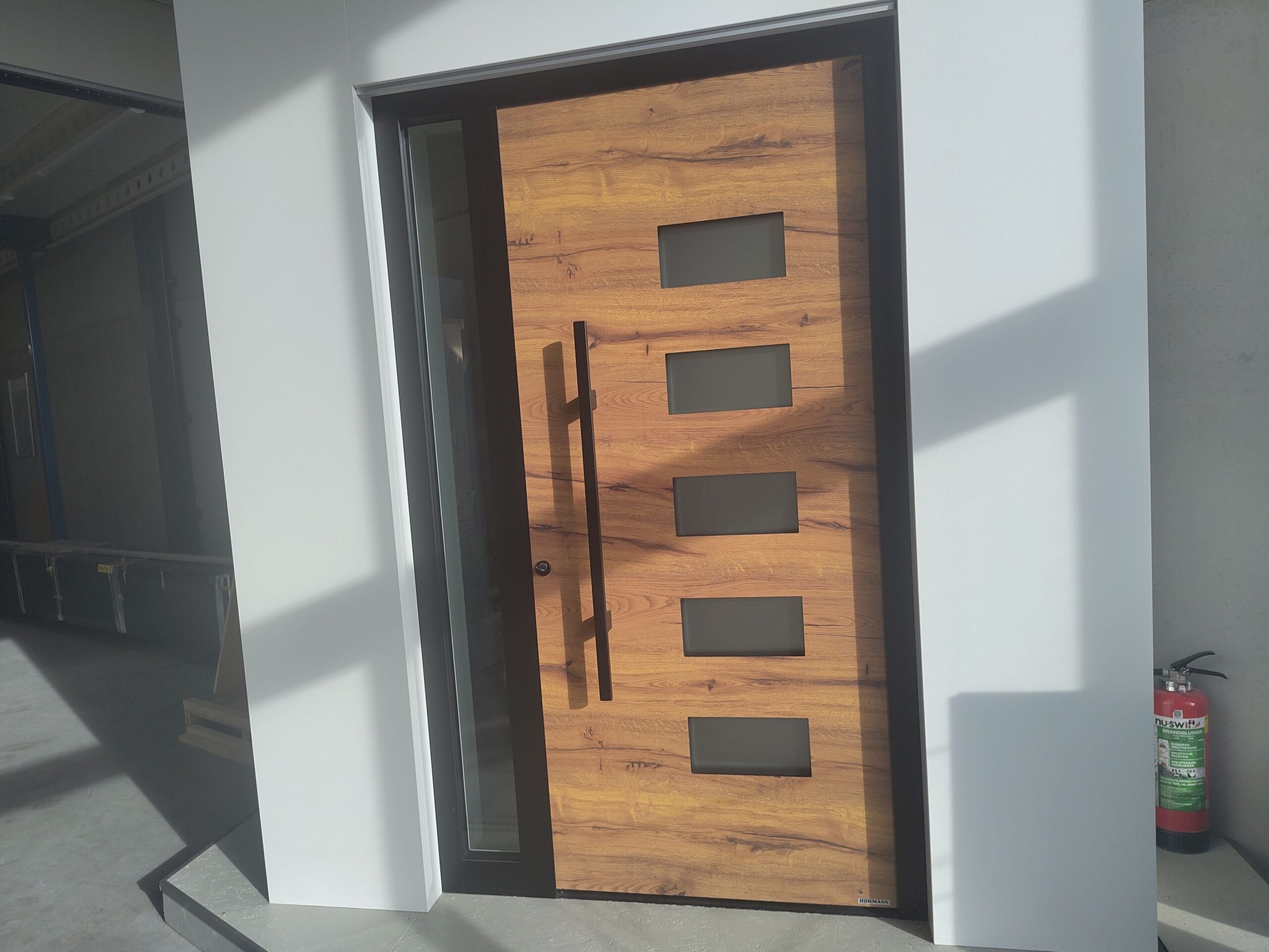 Houten voordeur in showroom met smal zijraam, verticale handgreep en vier rechthoekige ramen