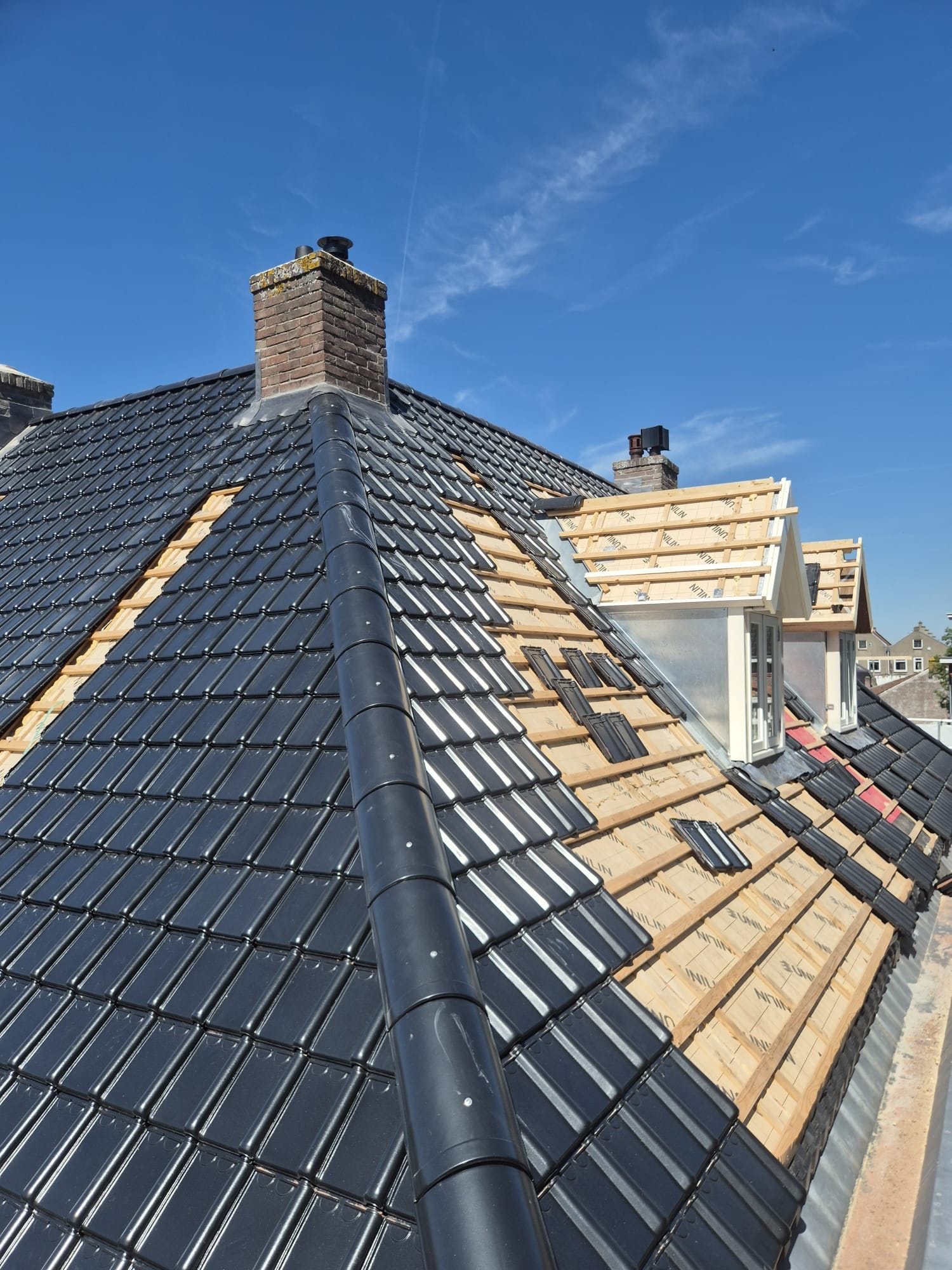 dak met deels vernieuwde dakpannen en zicht op dakkapellen tijdens renovatie