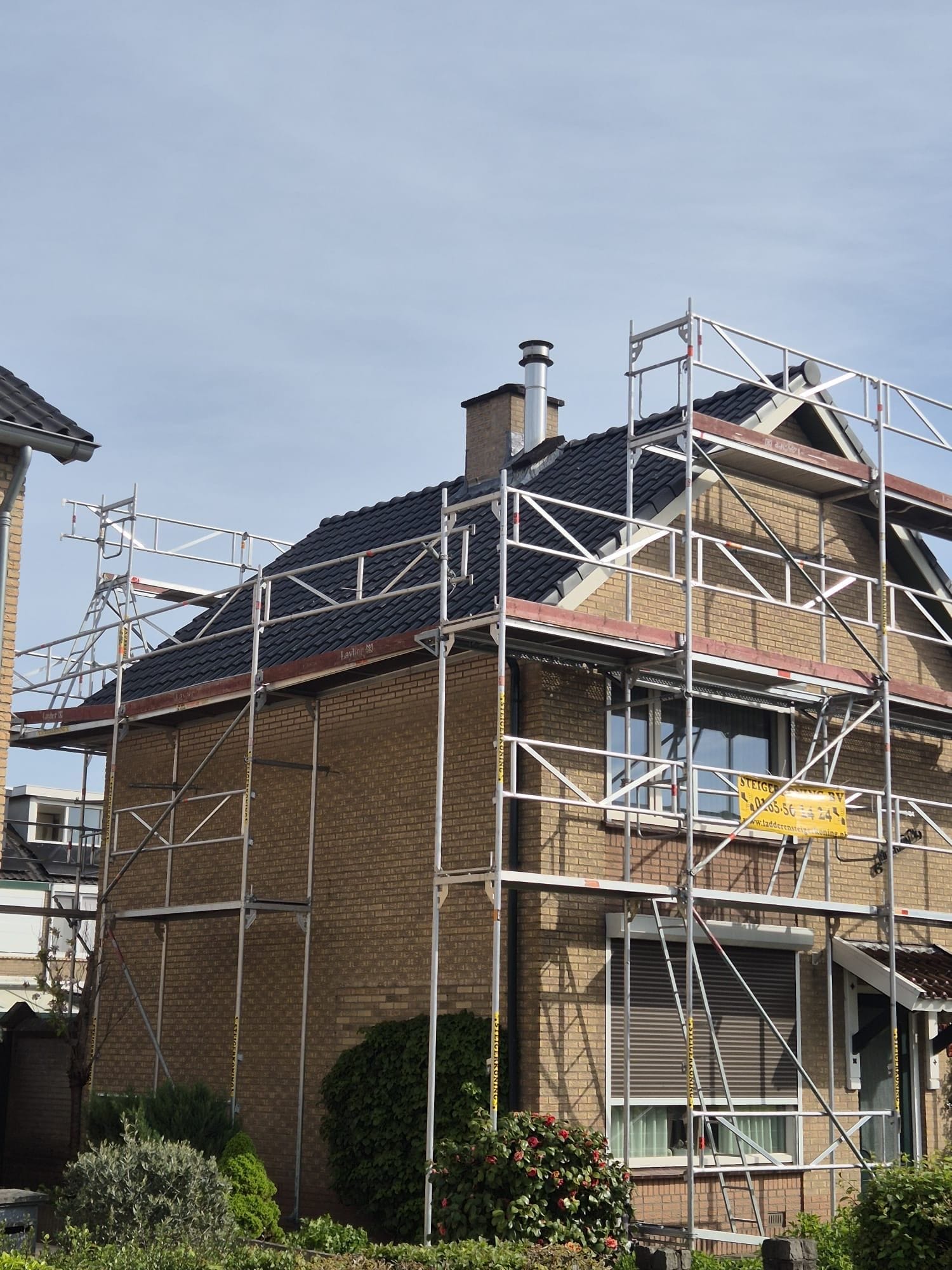 Woonhuis met steiger bij dakrenovatie, zicht op nieuw dak en schoorsteen