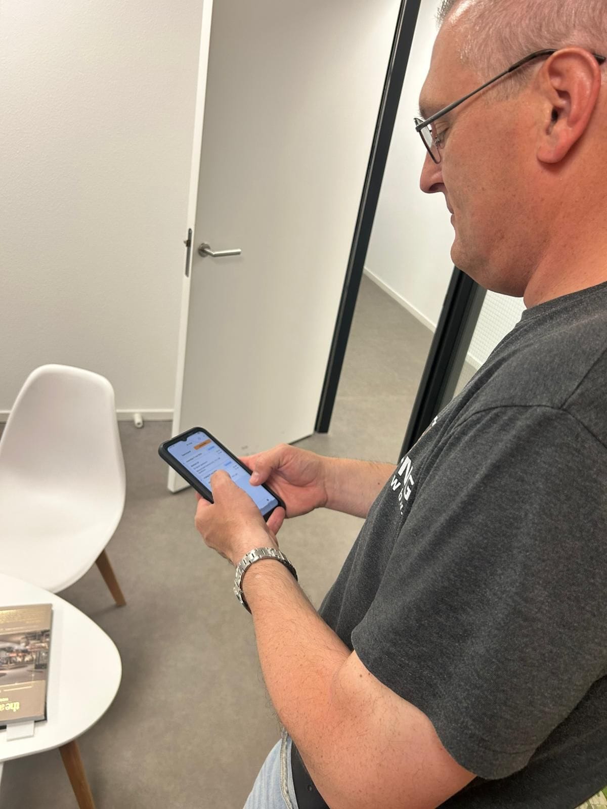 Monteur van De Jong EKW bekijkt werkorder op smartphone in kantooromgeving
