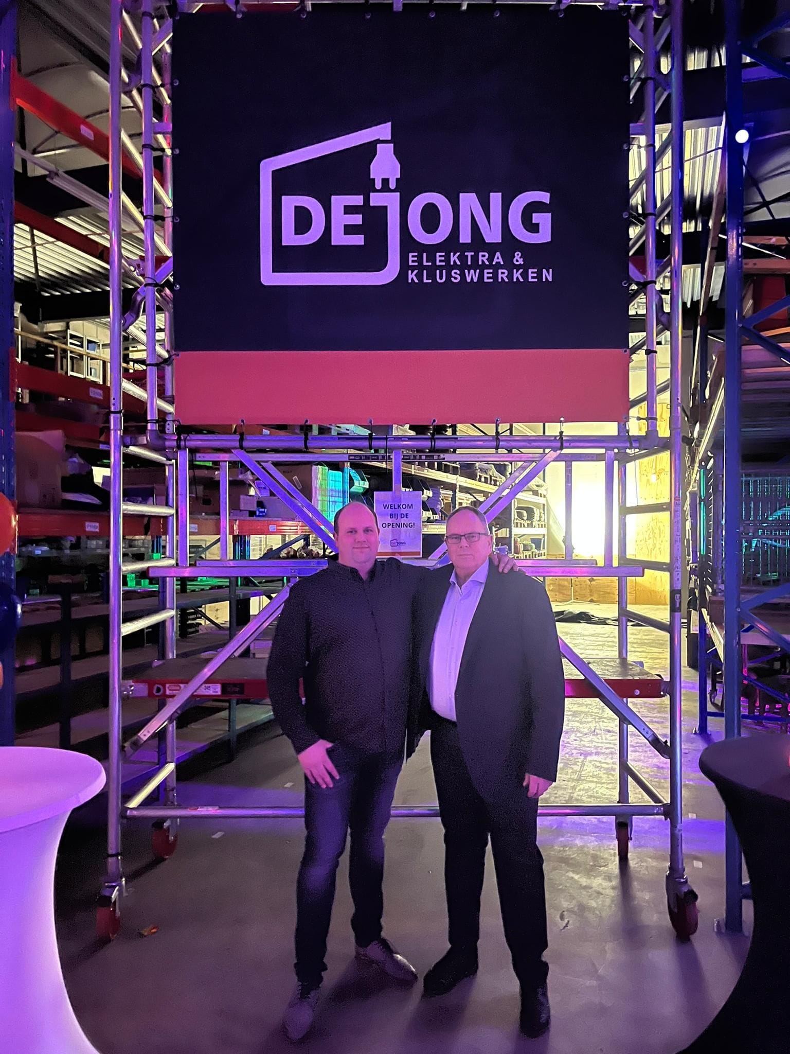 Twee mannen voor De Jong Elektra & Kluswerken logo in magazijn