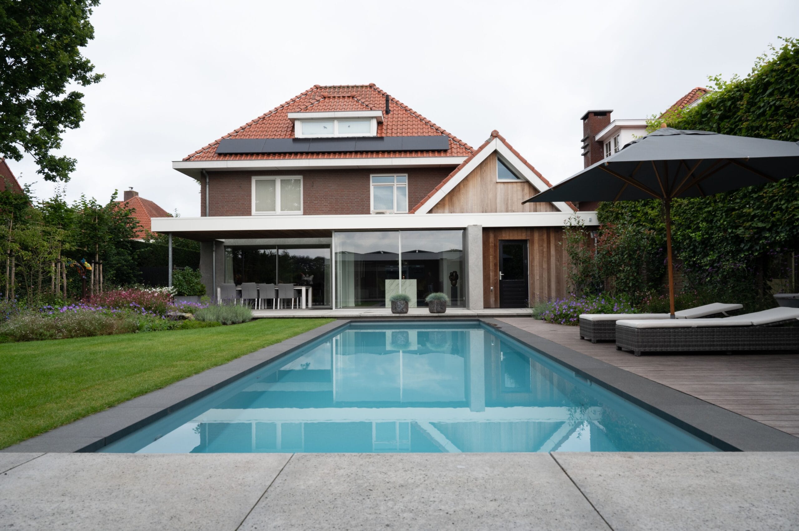 rechthoekig zwembad met terras en modern huis op de achtergrond