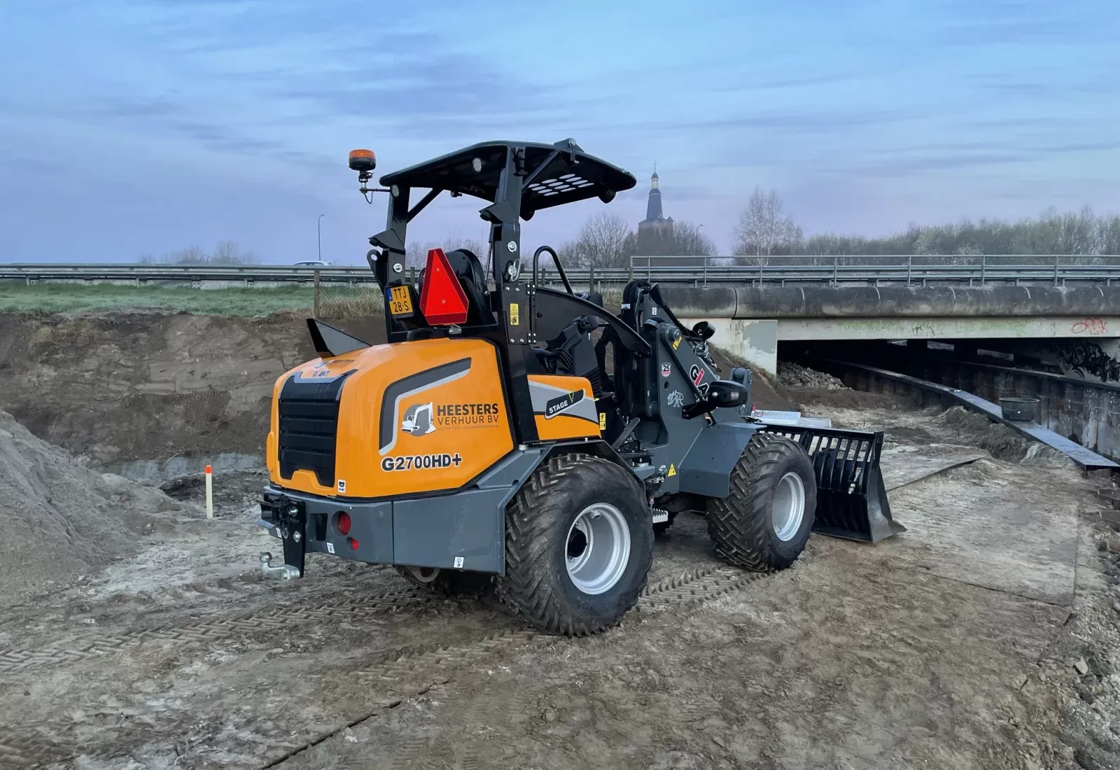 Oranje minilader met Heesters Verhuur logo op bouwplaats