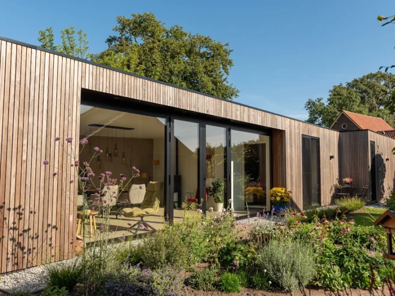 Houten bijgebouw met glazen deuren en een bloeiende tuin