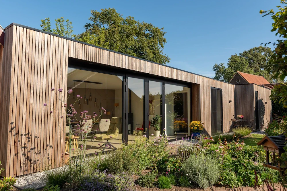 Houten bijgebouw met glazen deuren en een bloeiende tuin